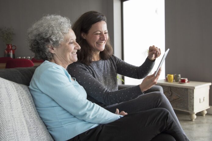 Happy elderly woman and her daughter browsing on tablet computer Hábitos precoces moldam envelhecimento saudável